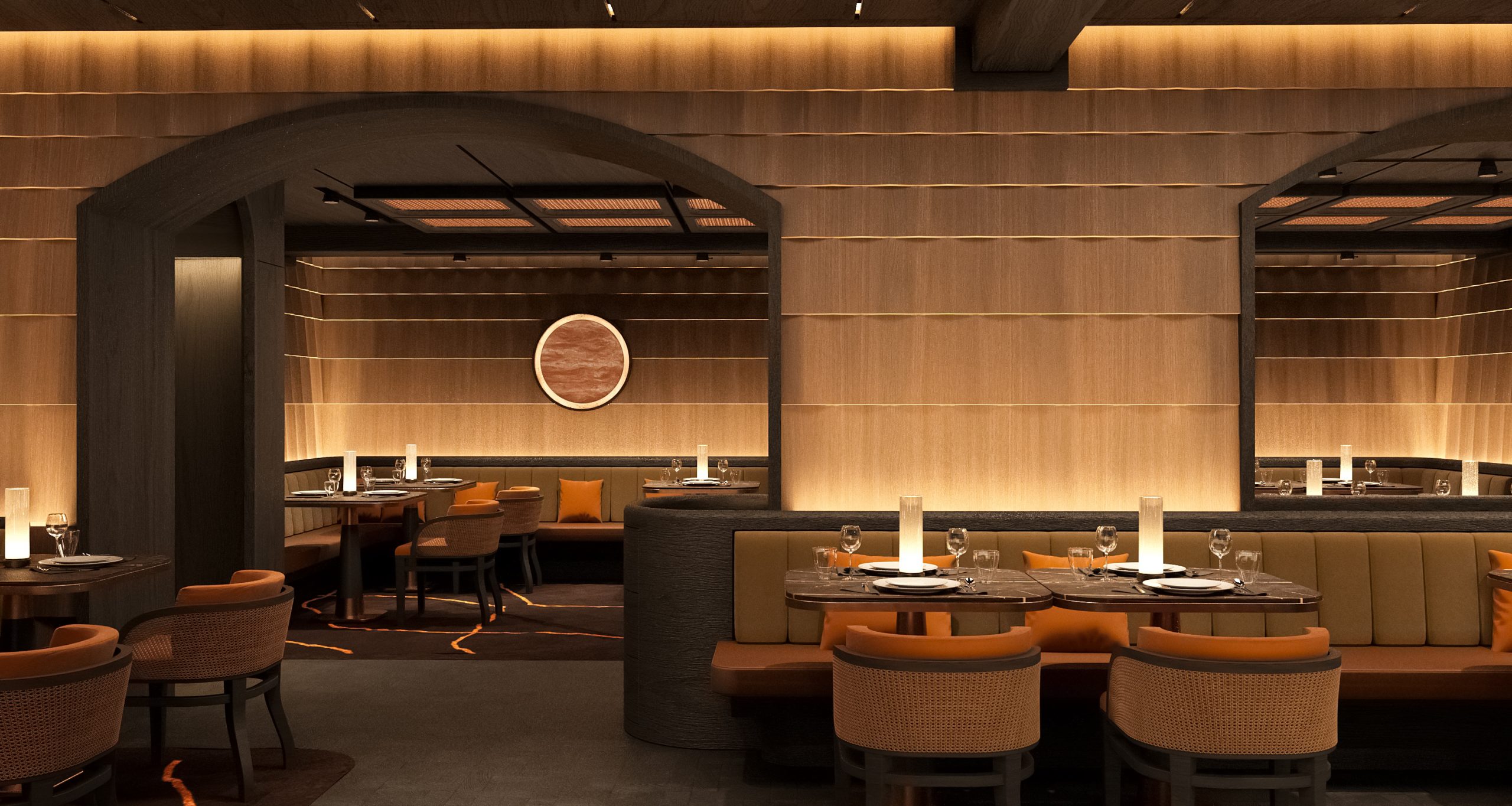 Ein modernes Restaurant mit warmer Beleuchtung, Holzwänden, runden Tischen zum Essen, gepolsterten Stühlen und gewölbten Türöffnungen. Ein rundes Kunstwerk hängt an der Wand in einer gemütlichen Nische.